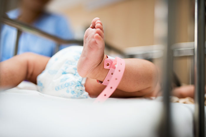 Baby lying in hospital crib with a pink ID band around its ankle. Baby lying in hospital crib with a pink ID band around its ankle.
