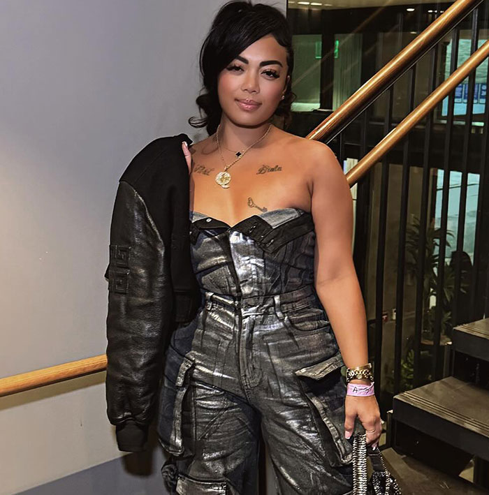 Woman in a metallic jumpsuit and jacket on stairs, related to flight attendant's lingerie business and GoFundMe support. Woman in a metallic jumpsuit and jacket on stairs, related to flight attendant's lingerie business and GoFundMe support.