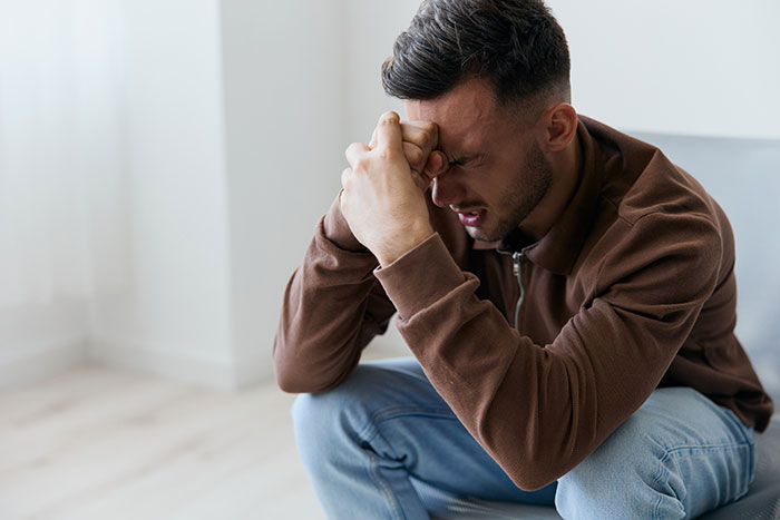 A man in emotional distress sitting on a couch, wearing a brown jacket and jeans. A man in emotional distress sitting on a couch, wearing a brown jacket and jeans.