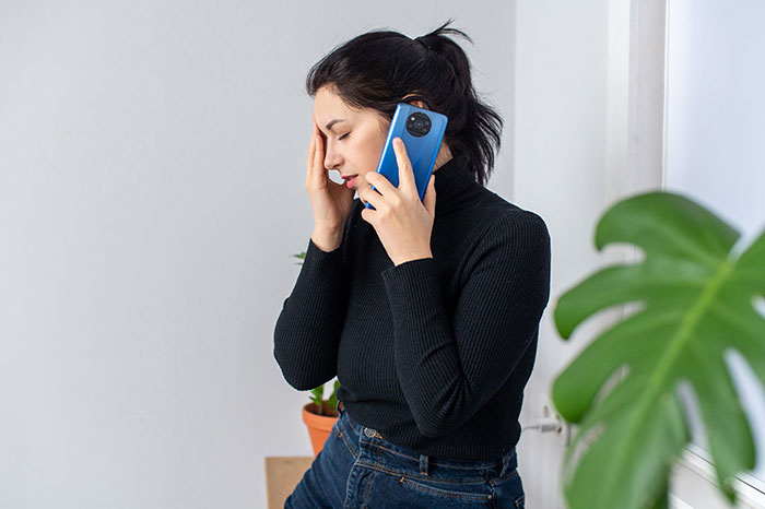 Woman in black sweater on phone, looking stressed near a plant. Woman in black sweater on phone, looking stressed near a plant.