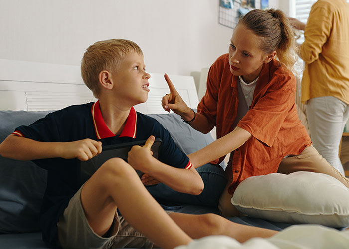 Woman scolding a boy on a couch, conveying family tension and disagreement, with another adult in the background. Woman scolding a boy on a couch, conveying family tension and disagreement, with another adult in the background.