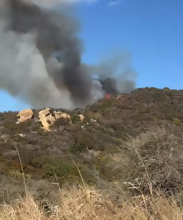 Thick smoke rises from a hillside fire in La Palisades under a clear blue sky. Thick smoke rises from a hillside fire in La Palisades under a clear blue sky.
