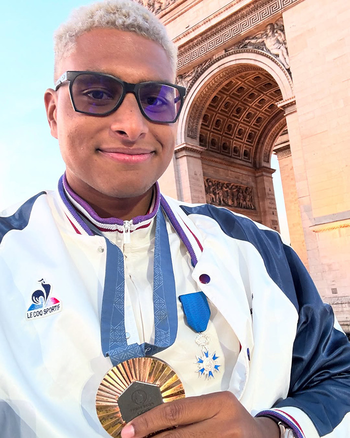 Athlete in Paris holding a medal, standing near a historic arch, wearing dark glasses and a sports jacket. Athlete in Paris holding a medal, standing near a historic arch, wearing dark glasses and a sports jacket.