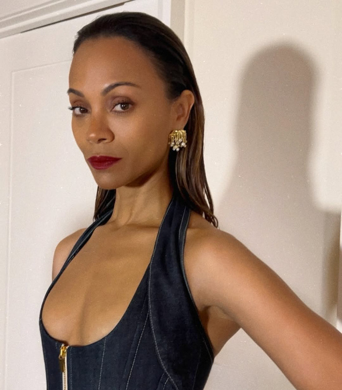 I don't know who this is. A person in a sleeveless denim outfit, red lipstick, and gold earrings, standing against a white wall. I don't know who this is. A person in a sleeveless denim outfit, red lipstick, and gold earrings, standing against a white wall.