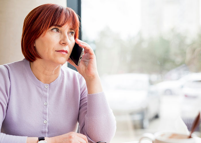 Woman with red hair in a lavender sweater, talking on the phone, sitting by a window, possibly contemplating an influencer request. Woman with red hair in a lavender sweater, talking on the phone, sitting by a window, possibly contemplating an influencer request.