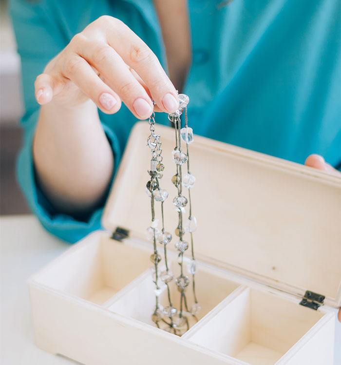 Woman in blue shirt holding jewelry over an open box, focusing on elegance and detail. Woman in blue shirt holding jewelry over an open box, focusing on elegance and detail.