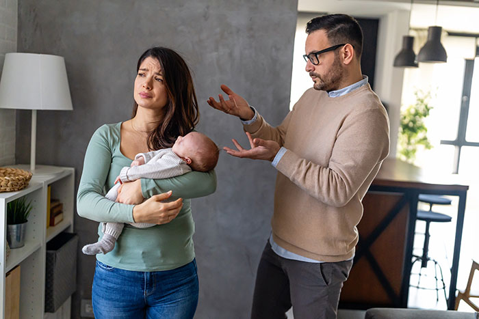 Man and woman argue at home while holding baby, referencing "choice of baby name" discussion. Man and woman argue at home while holding baby, referencing "choice of baby name" discussion.