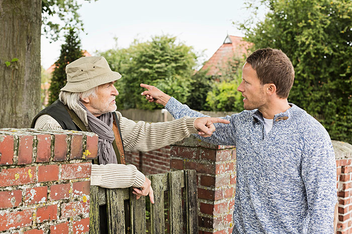 Neighbors arguing outside near a brick fence about light complaints. Neighbors arguing outside near a brick fence about light complaints.