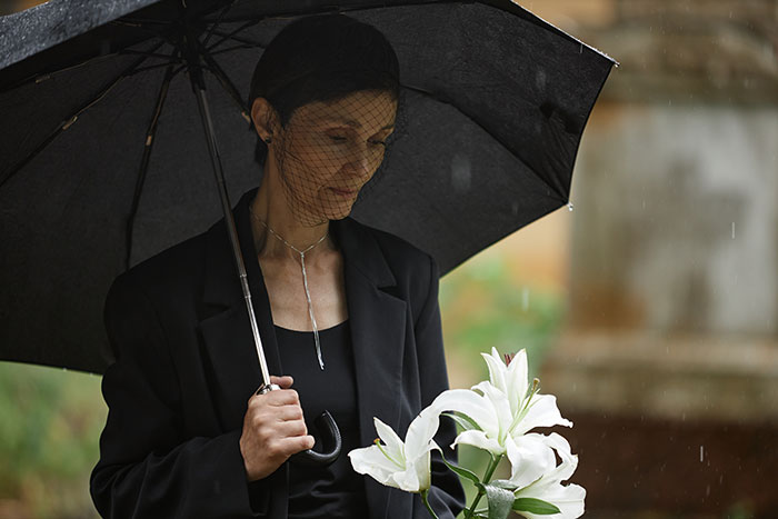 A woman in mourning attire holds lilies and an umbrella at a funeral, related to inheritance issue. A woman in mourning attire holds lilies and an umbrella at a funeral, related to inheritance issue.