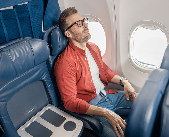 Man sitting alone on an airplane, wearing glasses and a red shirt, looking relaxed. Man sitting alone on an airplane, wearing glasses and a red shirt, looking relaxed.