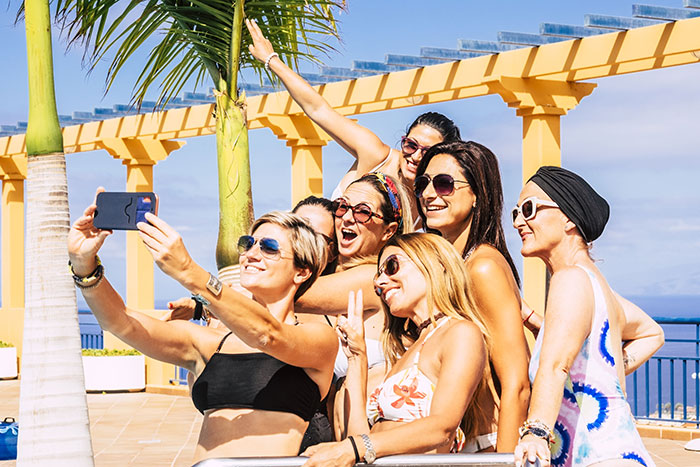 Group of women in swimsuits taking a selfie on vacation near palm trees, enjoying sunny weather. Group of women in swimsuits taking a selfie on vacation near palm trees, enjoying sunny weather.