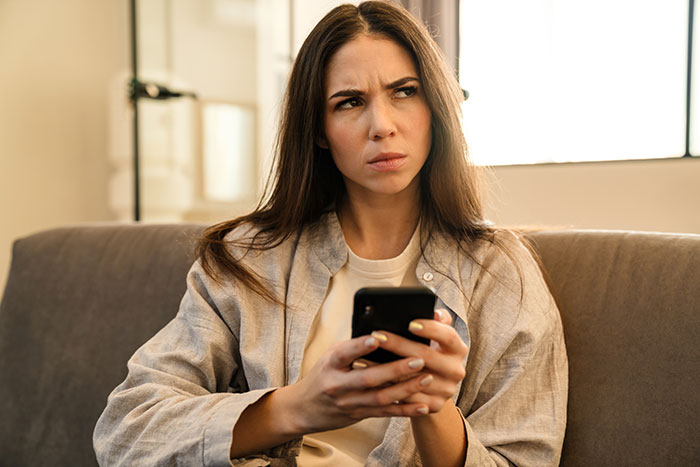 Woman sitting on a couch, holding a phone, looking puzzled about inheritance. Woman sitting on a couch, holding a phone, looking puzzled about inheritance.