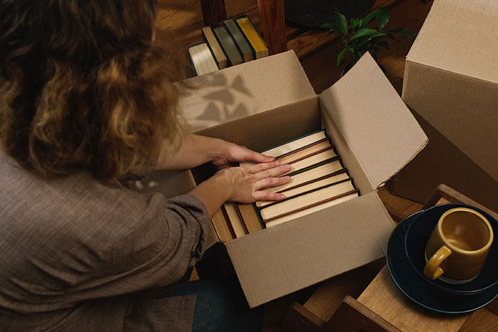 Person packing books into a box next to a mug, related to inheritance discussion. Person packing books into a box next to a mug, related to inheritance discussion.