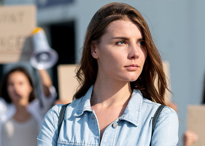 Woman looks serious, standing outside with protest signs visible, highlighting a Planned Parenthood visit for cancer screening. Woman looks serious, standing outside with protest signs visible, highlighting a Planned Parenthood visit for cancer screening.