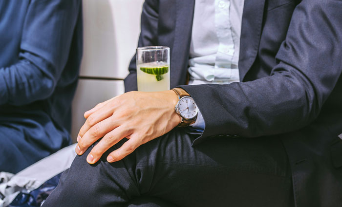 Man in suit holding a cocktail, seated, highlighting "coworkers' game" context, and wearing a wristwatch. Man in suit holding a cocktail, seated, highlighting "coworkers' game" context, and wearing a wristwatch.