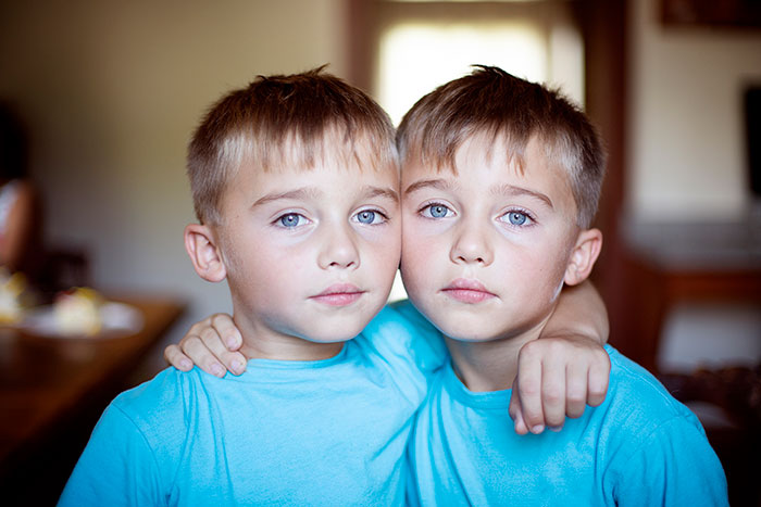 Twins in matching blue shirts with arms around each other, highlighting different approaches to dressing twins. Twins in matching blue shirts with arms around each other, highlighting different approaches to dressing twins.