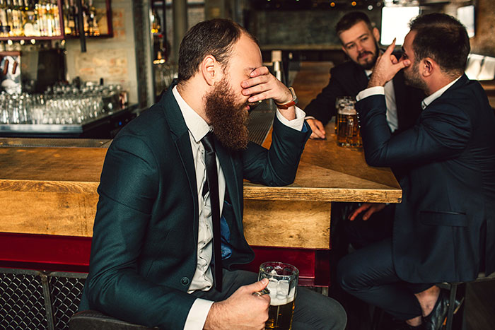 Three men in suits sitting at a bar, looking serious, with one covering his face; concept of homophobic confrontation. Three men in suits sitting at a bar, looking serious, with one covering his face; concept of homophobic confrontation.