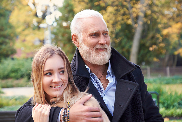 Older man and young woman smiling outdoors, showcasing age-gap relationships. Older man and young woman smiling outdoors, showcasing age-gap relationships.