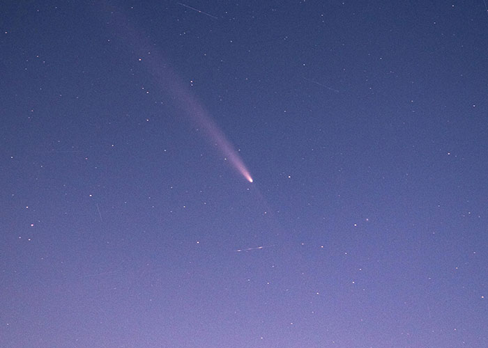A comet streaks across a starry night sky, its tail glowing brightly.