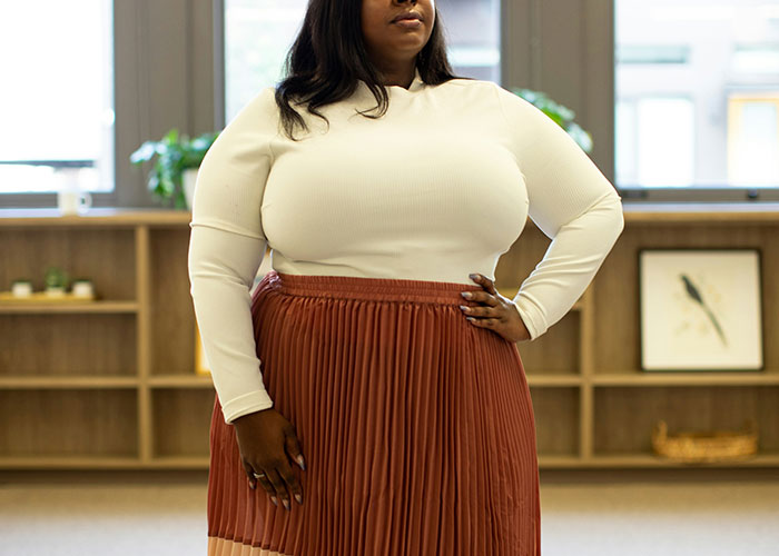 Person standing indoors wearing a white top and red skirt, highlighting issues related to being overweight.
