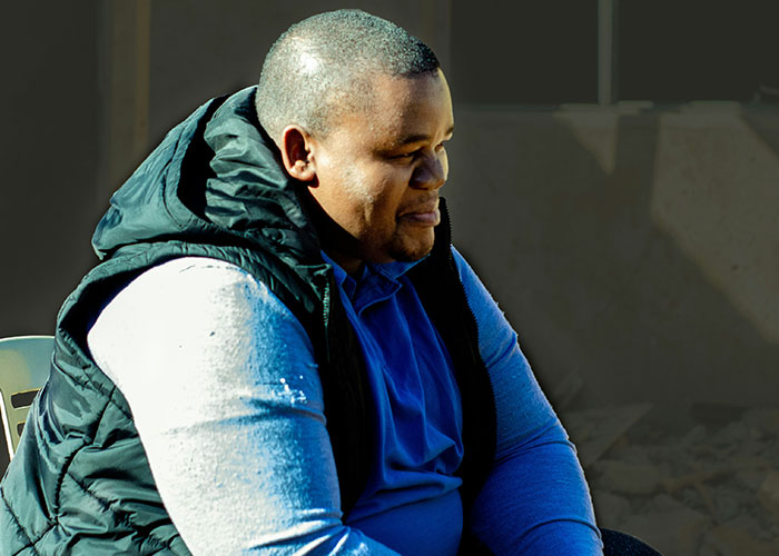 Man in a blue shirt and black vest sitting outdoors, highlighting challenges of being overweight.