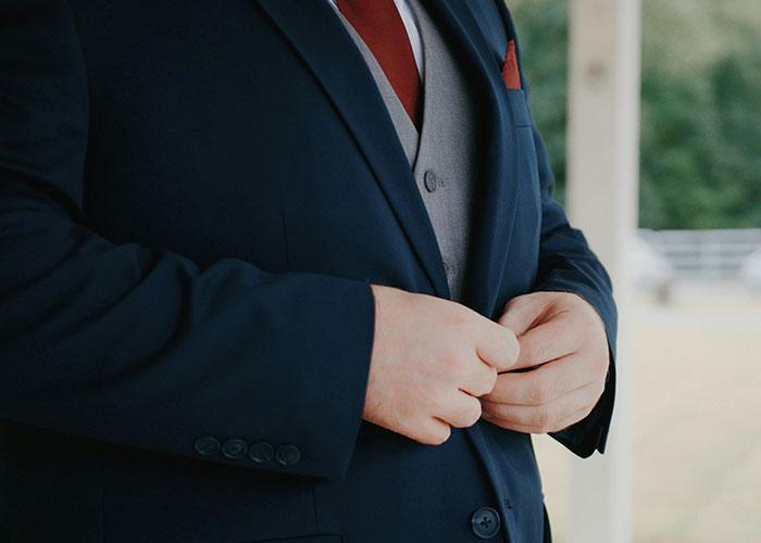 Man in a dark suit buttoning his jacket, related to issues faced when being overweight.