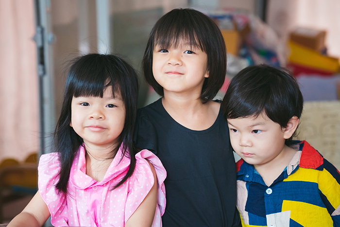 Three young children smiling and posing indoors, showcasing family bonds. Three young children smiling and posing indoors, showcasing family bonds.