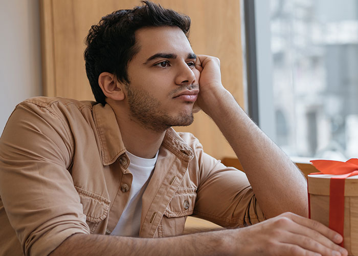 Man looking upset next to a gift box, embodying an ungrateful birthday meltdown. Man looking upset next to a gift box, embodying an ungrateful birthday meltdown.