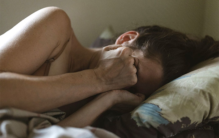 A woman lying in bed, covering her face with her hands, reflecting on a personal moment about divorce papers and relationships. A woman lying in bed, covering her face with her hands, reflecting on a personal moment about divorce papers and relationships.