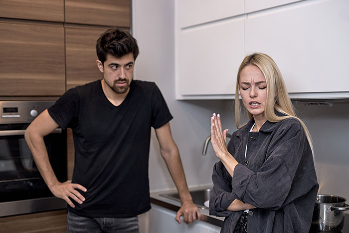 Man in a kitchen comments on laundry, woman reacts angrily, illustrating post-surgery relationship tension. Man in a kitchen comments on laundry, woman reacts angrily, illustrating post-surgery relationship tension.