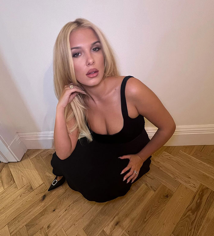 Young woman with a bold new look, sitting on a wooden floor in a black dress, showcasing her blonde hair and sassy style. Young woman with a bold new look, sitting on a wooden floor in a black dress, showcasing her blonde hair and sassy style.