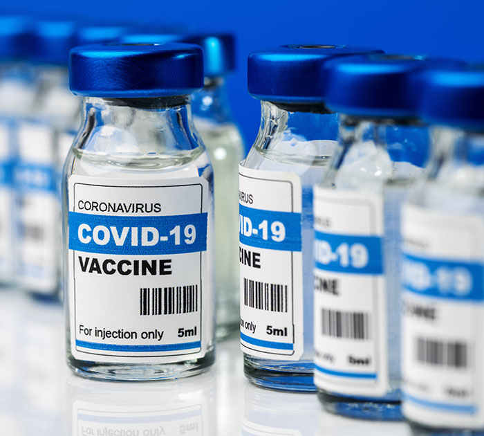 Covid vaccines vials with blue caps and labels, focus on foreground vial. Covid vaccines vials with blue caps and labels, focus on foreground vial.