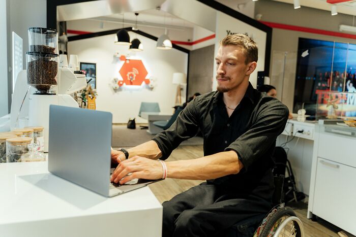 Man in wheelchair working on a laptop in a modern office, illustrating people and their genetic blessings and weaknesses.