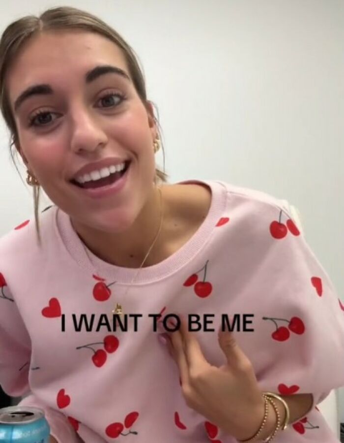 Woman wearing a pink cherry-patterned shirt with "I want to be me" text, smiling confidently. Woman wearing a pink cherry-patterned shirt with "I want to be me" text, smiling confidently.