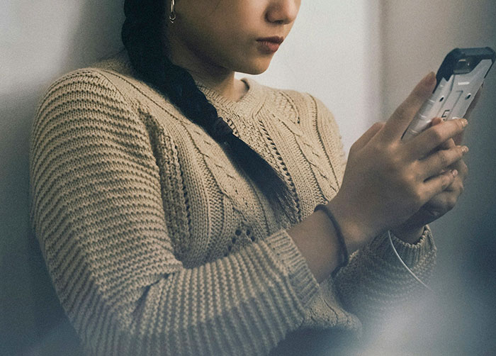 Woman in a knitted sweater looking concerned while checking her phone, symbolizing relationship tension over a coworker's game. Woman in a knitted sweater looking concerned while checking her phone, symbolizing relationship tension over a coworker's game.