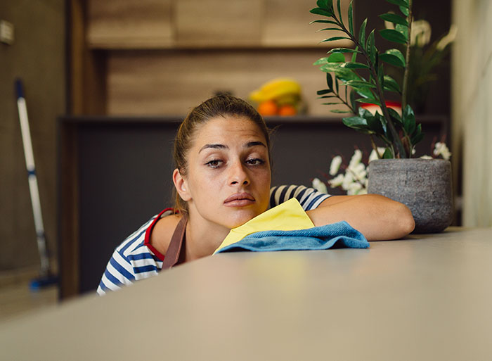 Woman looking tired while cleaning, embodying frustration over houseguests treating her home like a hotel. Woman looking tired while cleaning, embodying frustration over houseguests treating her home like a hotel.