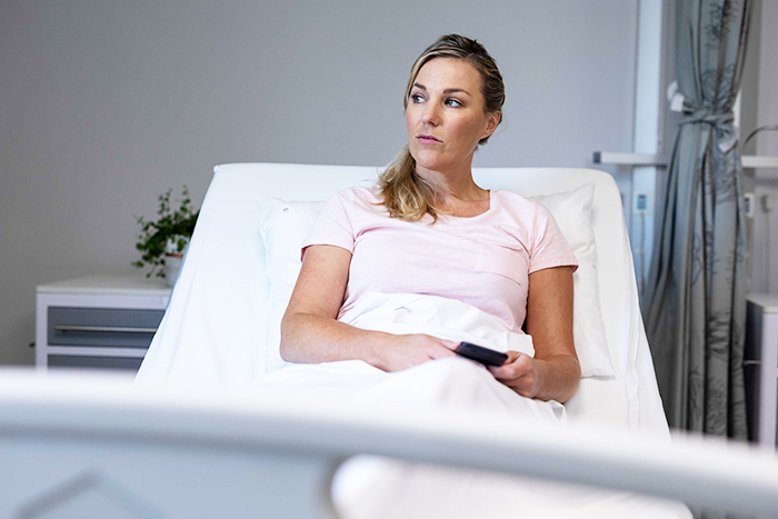 Woman in a hospital bed looking concerned while holding a remote, relating to a marriage issue. Woman in a hospital bed looking concerned while holding a remote, relating to a marriage issue.