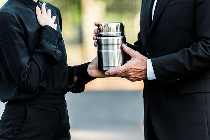 Two people holding an urn, symbolizing family tensions over mother's ashes. Two people holding an urn, symbolizing family tensions over mother's ashes.