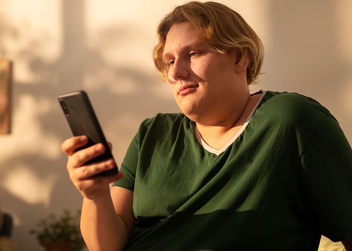 Individual in a green shirt looking at a smartphone, contemplating experiences related to being overweight.