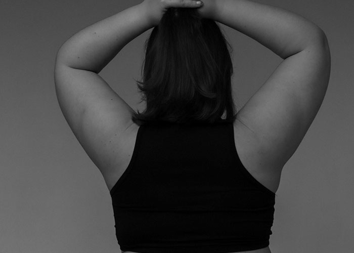 Person wearing a sleeveless top, seen from the back, arms raised, representing challenges of being overweight.