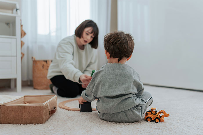 Woman playing with a child on a carpet, with toys and a basket in the background, related to babysitting. Woman playing with a child on a carpet, with toys and a basket in the background, related to babysitting.