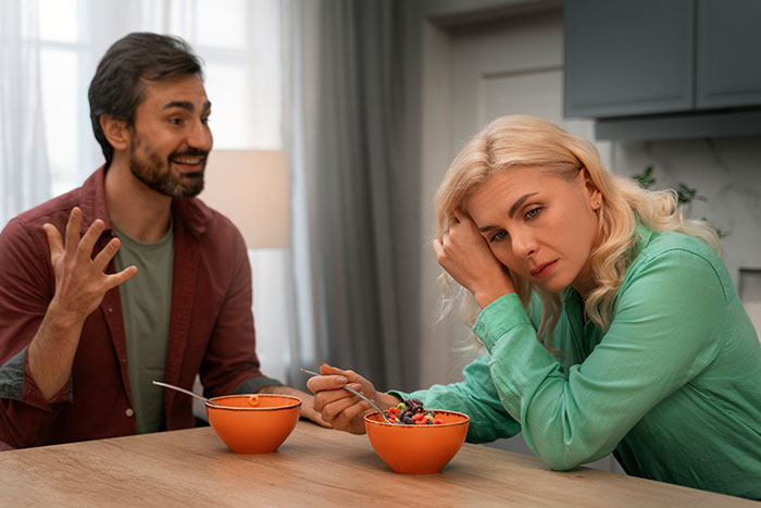 Man gesturing while speaking to woman with cereal at table, highlighting relationship tension. Man gesturing while speaking to woman with cereal at table, highlighting relationship tension.