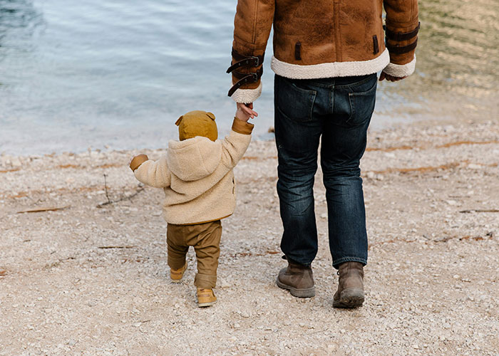 Adult and child holding hands by the water, illustrating young people and affordability concerns for having kids. Adult and child holding hands by the water, illustrating young people and affordability concerns for having kids.