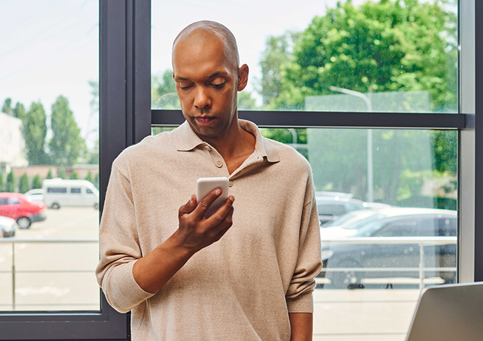 Man looking at his phone, decision impacting marriage, in a bright room with a view of parked cars and trees. Man looking at his phone, decision impacting marriage, in a bright room with a view of parked cars and trees.