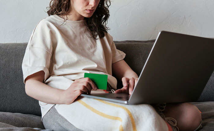 Woman holding a credit card, typing on a laptop, highlighting online review actions. Woman holding a credit card, typing on a laptop, highlighting online review actions.