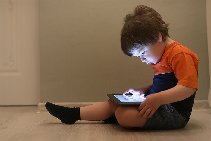Child focused on tablet in a dim room, illustrating concerns of iPad kids. Child focused on tablet in a dim room, illustrating concerns of iPad kids.