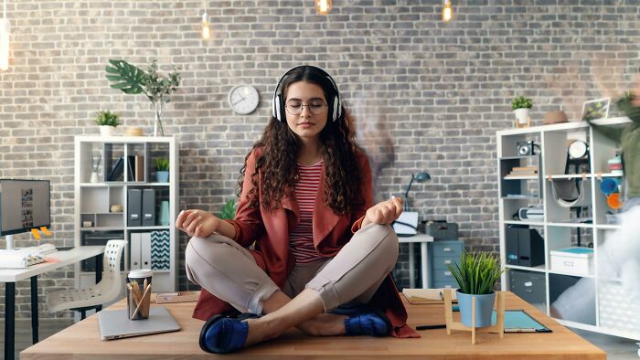 Person meditating on a desk, using headphones, amid office decor, representing genetic blessings and personal balance techniques.