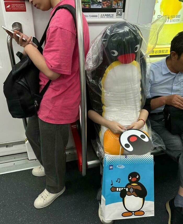 Person in a penguin costume sits on subway, surrounded by commuters. Unique scene embodying cultureavenue creativity.