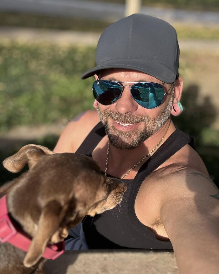 Man in sunglasses and cap joyfully reunited with his lost dog, wearing a pink collar, outdoors. Man in sunglasses and cap joyfully reunited with his lost dog, wearing a pink collar, outdoors.