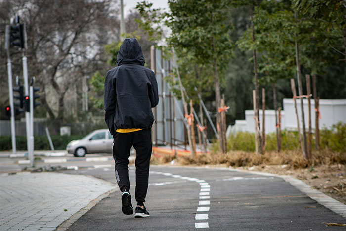 Teen in a black hoodie walking on a path, surrounded by trees, used to depict fake account creation scenario. Teen in a black hoodie walking on a path, surrounded by trees, used to depict fake account creation scenario.